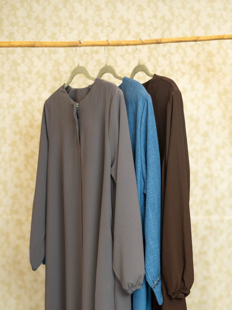 Grey, blue and brown Turkish abayas hanging on a bamboo rail